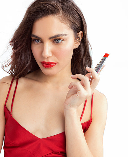 אישה לובשת שמלה אדומה, מחזיקה שפתון אדום.